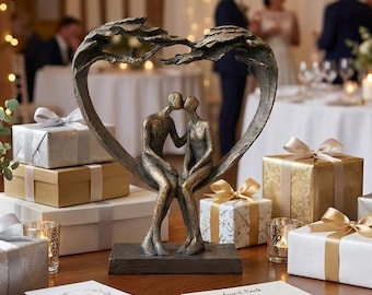 May include: A bronze-colored sculpture of a couple kissing, seated within a heart-shaped frame. The sculpture sits on a rectangular base. Gift boxes with gold and silver wrapping and ribbons surround the sculpture, suggesting a wedding or anniversary theme.