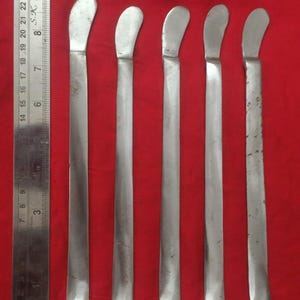 Pode incluir: Cinco ferramentas de metal prateado com pontas arredondadas, dispostas em fila sobre uma superfície vermelha. As ferramentas medem aproximadamente 38 cm de comprimento.