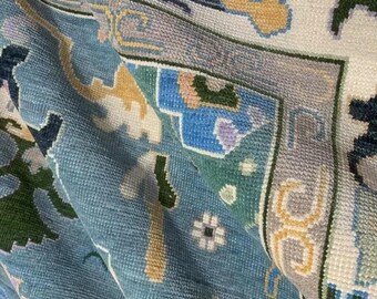 Könnte beinhalten: Nahaufnahme eines gewebten Teppichs mit detailliertem Muster. Der Teppich zeigt eine Kombination aus hellblau, creme, grün und gold. Das Design umfasst florale und geometrische Elemente und schafft eine strukturierte und dekorative Oberfläche.