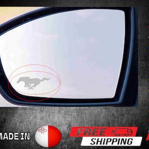 May include: A grey car side mirror with a silver running horse logo sticker. The sticker is in the centre of the mirror and is surrounded by a red circle.