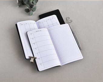 May include: Open black notebooks with grid paper, one showing a weekly calendar layout for February 2024. A silver pen and paper clips are nearby. The notebooks are on a grey surface.