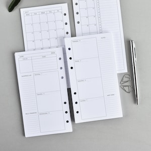 Op de afbeelding: Een set witte planner-inlays met zwarte inkt, voorzien van een maandkalender voor juli, een weekschema voor juni 2024 en een takenlijst. De pagina's hebben perforatiegaten aan de zijkant, vergezeld door een zilverkleurige metalen pen en twee clips.