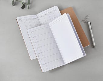 May include: Open notebooks with grid paper and weekly and monthly layouts. The notebooks have a brown cover and are next to a silver pen and paper clips. The pages are blank and ready to be filled with notes and plans.