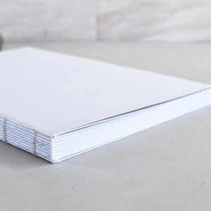 Puede incluir: Un cuaderno blanco en blanco con encuadernación cosida. Las páginas son nítidas y la cubierta es lisa. Perfecto para escribir, dibujar o llevar un diario. El cuaderno tiene un diseño sencillo y elegante.