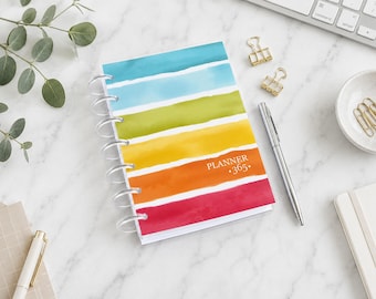 May include: A disc-bound planner featuring a horizontal watercolor stripe pattern in shades of teal, light blue, lime green, yellow, orange, and magenta. The cover displays the white text PLANNER 365. The planner is bound with clear plastic discs.