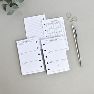 Può includere: Inserti per planner bianchi con testo nero, tra cui un calendario di giugno 2024 e layout settimanali per settembre 2024. Una penna d'argento e due fermagli d'argento sono presenti, su una superficie grigio chiaro.