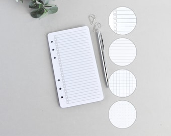 Può includere: Un inserto rettangolare in carta bianca con una colonna verticale di caselle di controllo e linee orizzontali, accompagnato da una penna in metallo argentato, due graffette argentate e quattro inserti circolari in carta con vari motivi.