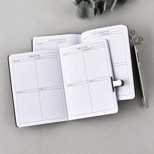 Op de afbeelding: Drie open zwarte notitieboekjes met geruit papier, gerangschikt op een grijze ondergrond. Eén notitieboekje wordt opengehouden met een zilveren clip. Een zilveren pen ligt naast de notitieboekjes. Groen is zichtbaar in de bovenhoek.