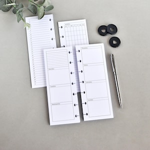 Può includere: Una collezione di inserti per planner bianchi con testo nero, inclusi layout giornalieri, settimanali e mensili. Sono presenti anche anelli neri e una penna d'argento. Gli inserti sono progettati per l'organizzazione e la pianificazione.