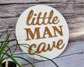 May include: White round wooden sign with the words "little man cave" in brown wood letters.