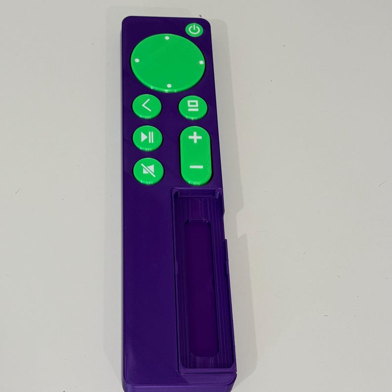 May include: A purple remote control with green buttons. The buttons include a power button, volume controls, and playback controls. The remote has a rectangular shape and a slot for batteries.