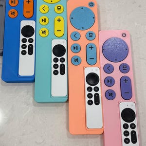 May include: A collection of colorful remote controls in blue, teal, peach, and pink. Each remote has a white control panel with black buttons. The buttons on the colored remotes are in contrasting colors like orange, yellow, and purple.