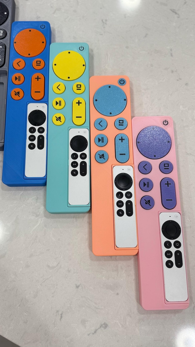May include: A collection of colorful remote controls in blue, teal, peach, and pink. Each remote has a white control panel with black buttons. The buttons on the colored remotes are in contrasting colors like orange, yellow, and purple.
