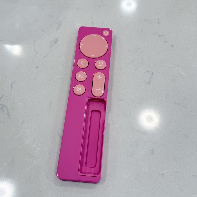 May include: A pink remote control with a circular navigation pad and various control buttons. The remote has a rectangular shape with a recessed area at the bottom. The buttons are a lighter shade of pink.