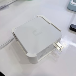 May include: A white electronic device with a U-shaped logo on top. The device has a rectangular shape with rounded corners and a two-prong plug. White plastic trim is on the corners. A white cord is attached.