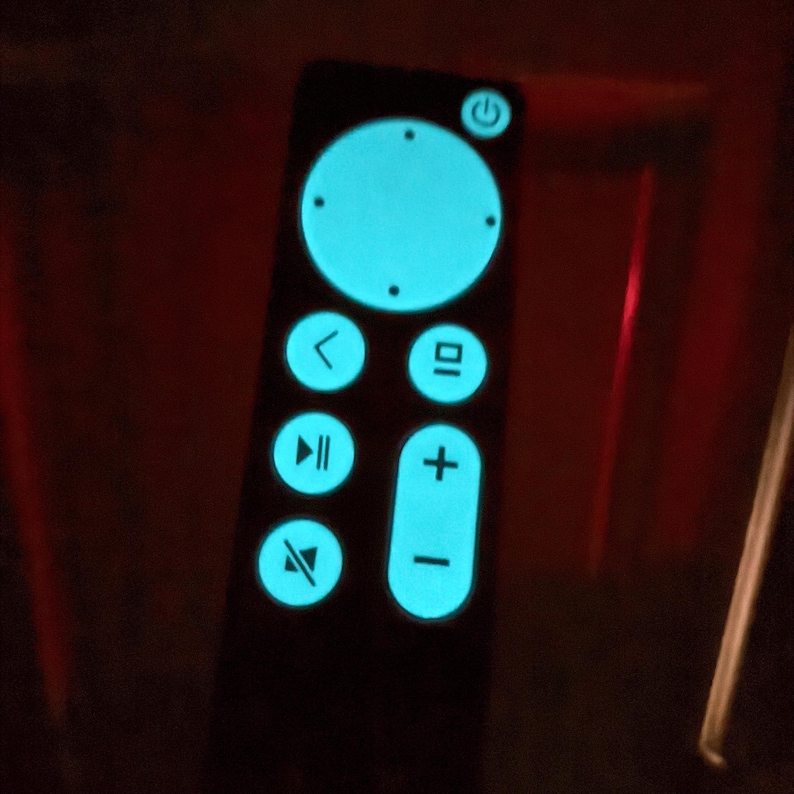 May include: A black remote control with glowing blue buttons. The buttons include a power button, directional arrows, play/pause, volume controls, and a number button. The remote is rectangular and appears to be made of plastic.