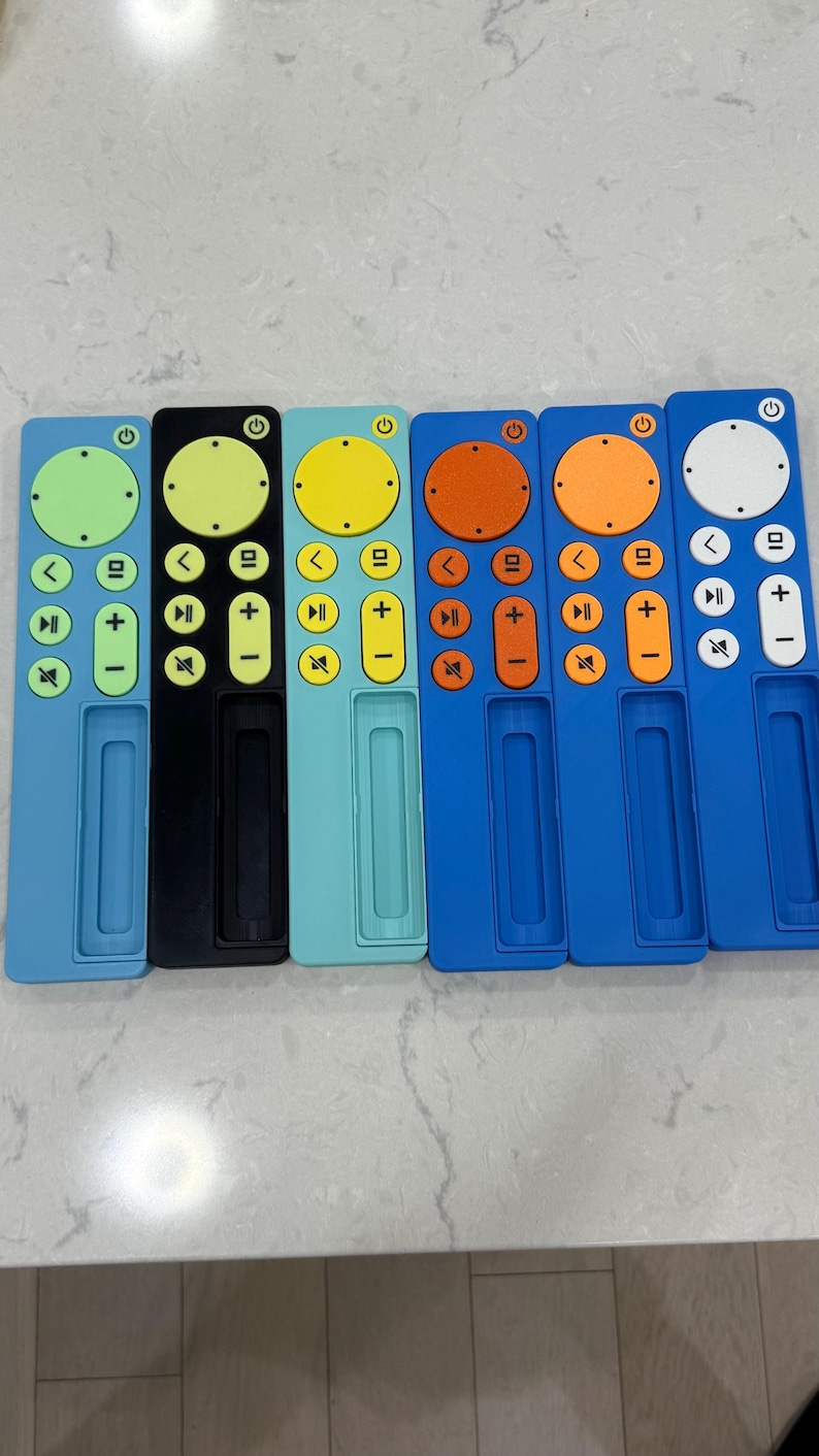 May include: A collection of six colorful remote control covers. The covers are in various colors, including light blue, black, teal, yellow, orange, and white. Each cover has a circular button and several directional buttons.