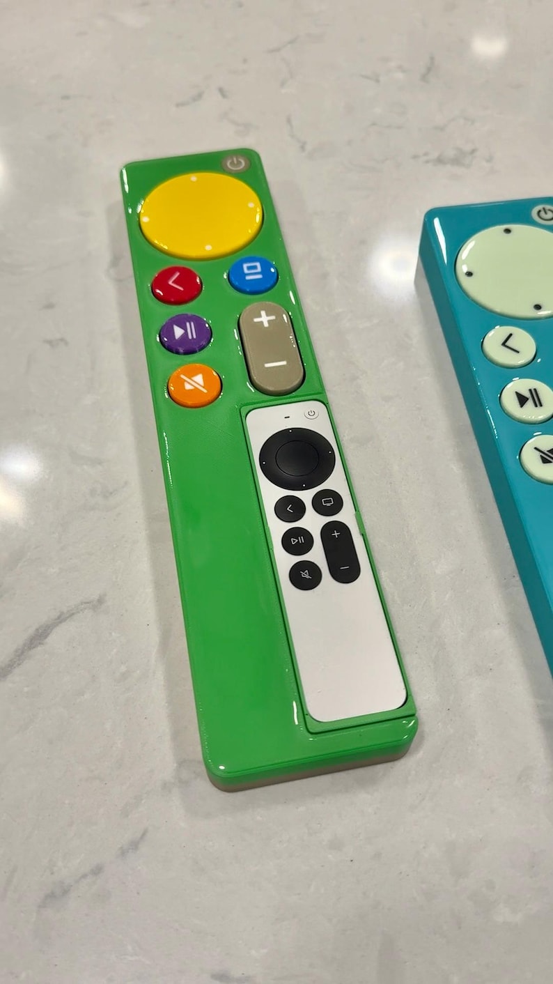 May include: Two colorful TV remotes. One is green with a yellow circle and multi-colored buttons. The other is teal with a light green circle and white buttons. Both have a white section with black buttons.