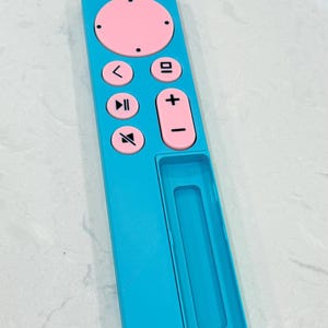 May include: A turquoise remote control with pink buttons and a power button. The remote has volume controls, a play/pause button, and a directional pad. The remote is rectangular with a recessed area on the bottom.