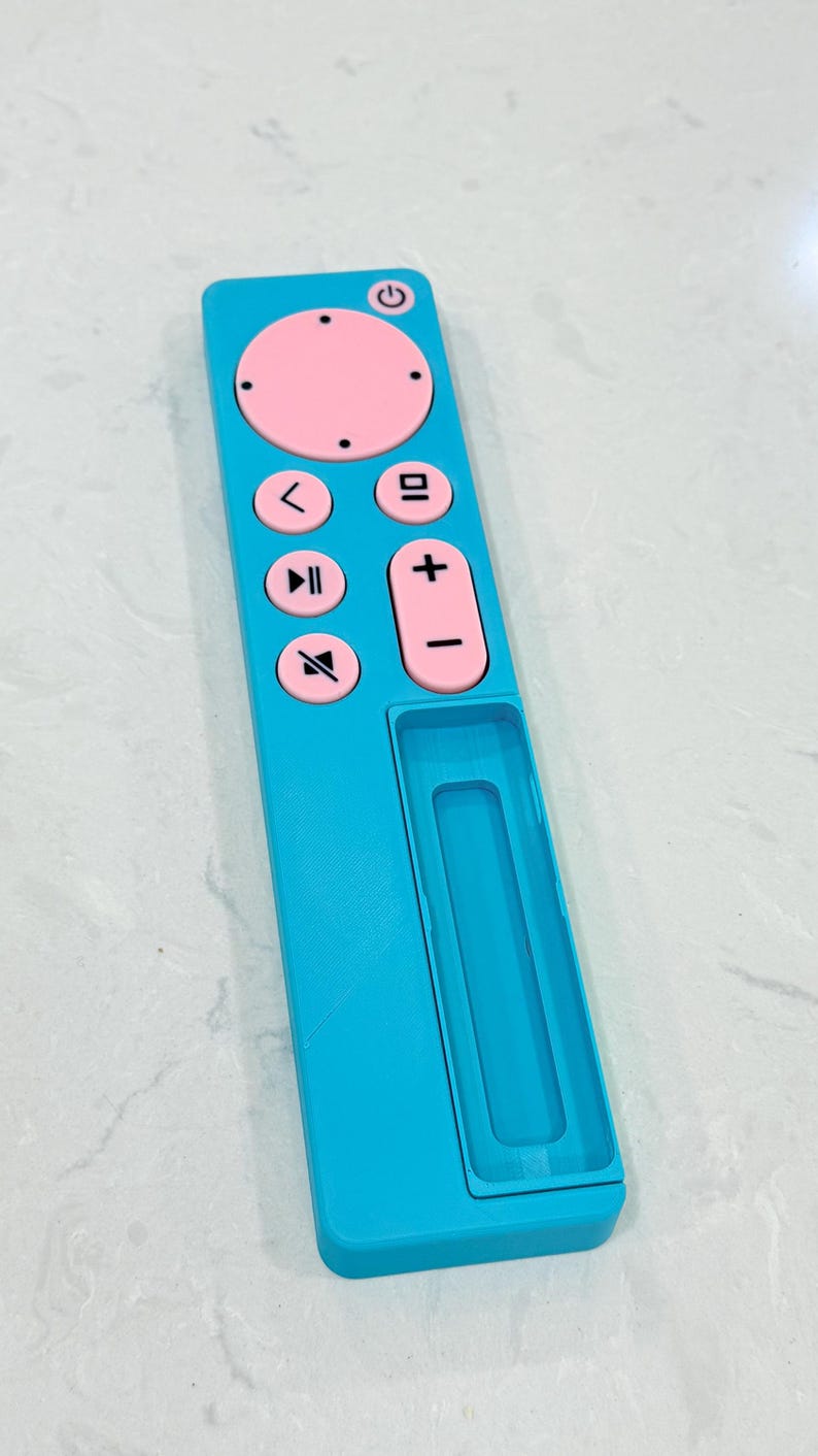 May include: A turquoise remote control with pink buttons and a power button. The remote has volume controls, a play/pause button, and a directional pad. The remote is rectangular with a recessed area on the bottom.