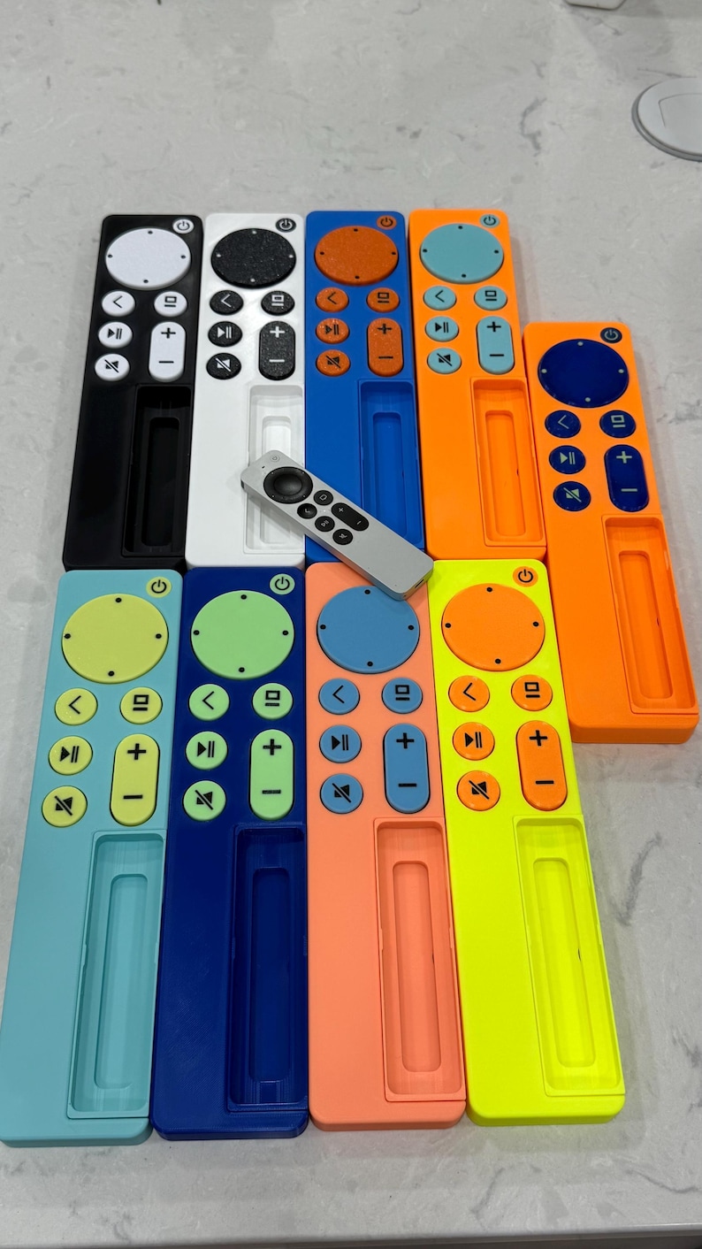 May include: A collection of colorful remote control cases in various shades, including black, white, blue, orange, and green. Each case has a rectangular design with button cutouts and a central slot. A silver remote is also present.