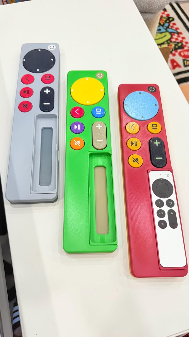May include: Three colorful remote controls in gray, green, and red. Each has a power button, directional controls, and volume buttons. The green remote has a yellow circle, and the red remote has a white remote attached.