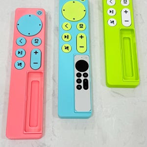May include: Three colorful remote control covers in pink, blue, and green. Each cover has a different color scheme for the buttons, including yellow, blue, and white. The covers are designed to fit a standard remote control.