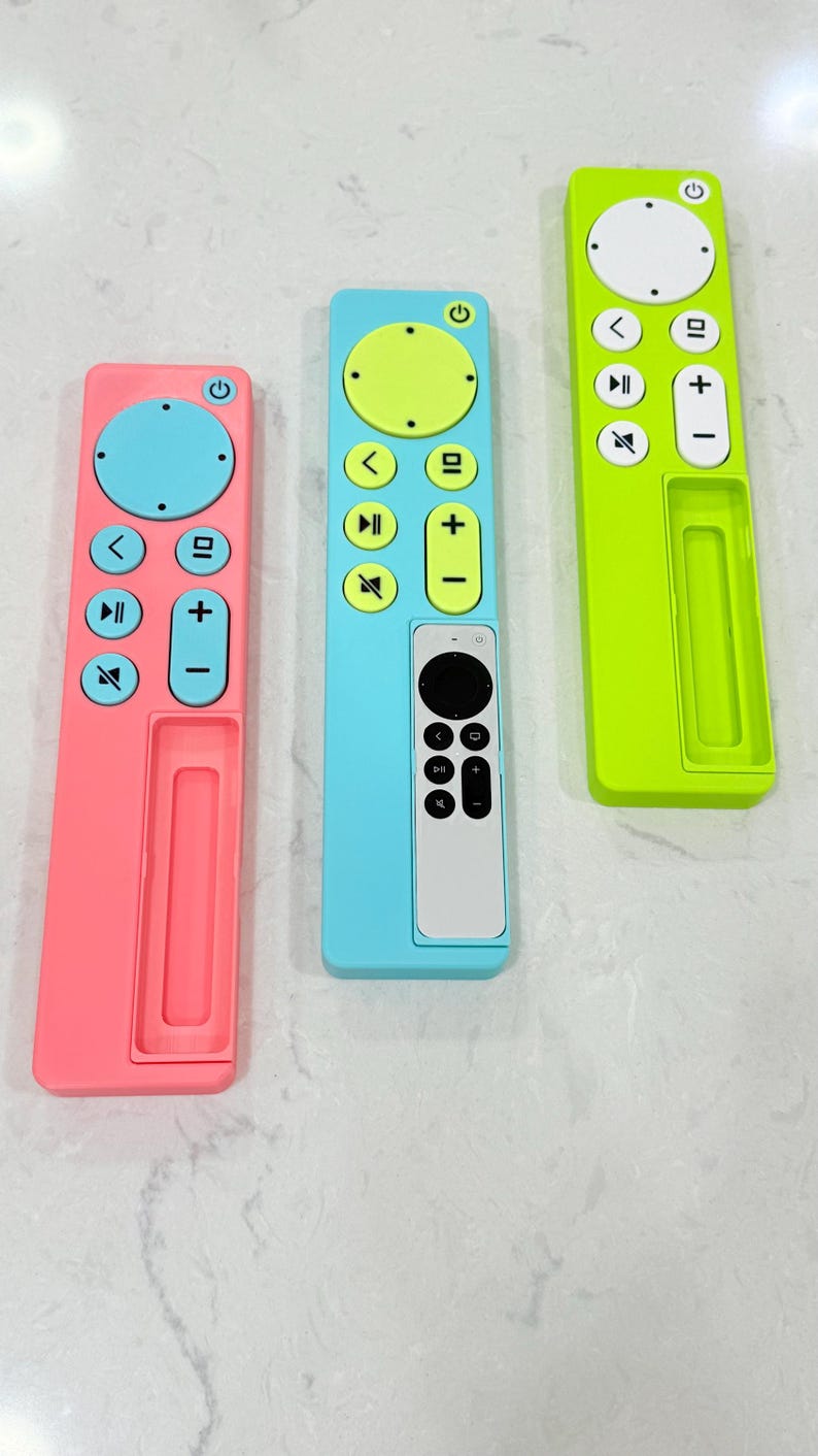 May include: Three colorful remote control covers in pink, blue, and green. Each cover has a different color scheme for the buttons, including yellow, blue, and white. The covers are designed to fit a standard remote control.