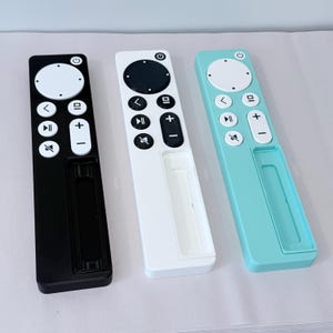 May include: Three remote controls in black, white, and teal. Each has a circular power button, a directional pad, and volume controls. The remotes have a sleek, minimalist design with a rectangular shape and a recessed area at the bottom.