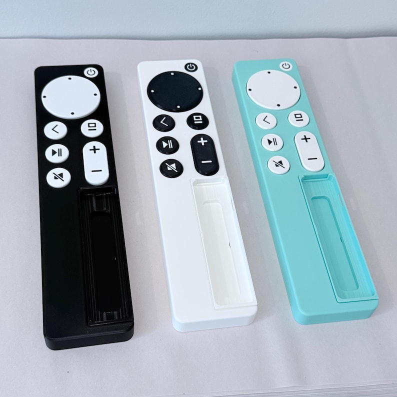 May include: Three remote controls in black, white, and teal. Each has a circular power button, a directional pad, and volume controls. The remotes have a sleek, minimalist design with a rectangular shape and a recessed area at the bottom.
