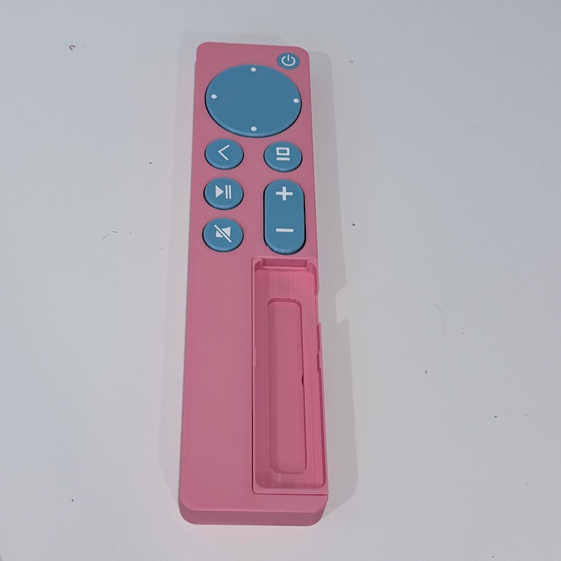 May include: A pink remote control with blue buttons. The remote has a circular button at the top, a directional pad, and volume controls. The design is sleek and modern, with a minimalist aesthetic.