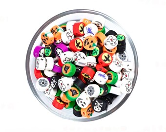 May include: A bowl filled with colourful Halloween themed beads. The beads are round and feature various Halloween icons such as ghosts, pumpkins, spiders, and skulls. The beads are in shades of orange, green, white, black, and purple.