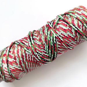 May include: A spool of red, green, white, and black twine. The twine is wound tightly around the spool.