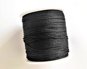 May include: A spool of black waxed cord, wound tightly on a white plastic bobbin.