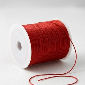May include: A spool of vibrant red thread, wound around a white plastic core. A length of the thread trails from the spool, contrasting against the white background. Suitable for crafts and sewing.