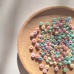 K&ouml;nnte beinhalten: Eine Holzschale gef&uuml;llt mit pastellfarbenen runden Perlen. Die Perlen sind in den Farben Rosa, Blau, Gr&uuml;n und Gelb.