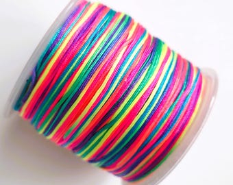 May include: A spool of rainbow coloured waxed cord. The cord is wound tightly around a clear plastic spool.