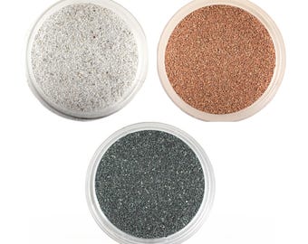 May include: Three small containers of sand, each with a different colour: white, brown, and grey.