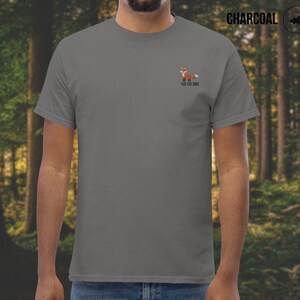 Puede incluir: Una camiseta gris antracita con un peque&ntilde;o gr&aacute;fico de zorro naranja y el texto "For Fox Sake" impreso en la parte delantera.