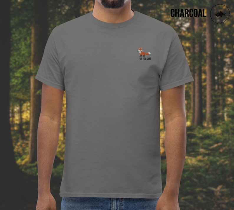 Puede incluir: Una camiseta gris antracita con un peque&ntilde;o gr&aacute;fico de zorro naranja y el texto "For Fox Sake" impreso en la parte delantera.