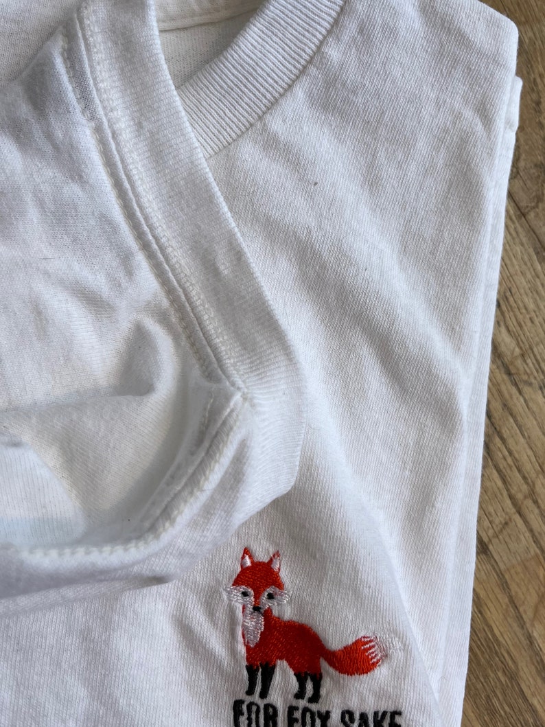 Puede incluir: Camiseta blanca con un zorro bordado en rojo y el texto "For Fox Sake" en negro.
