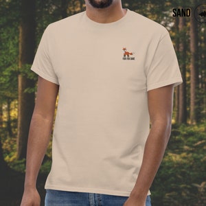 Puede incluir: Una camiseta beige con un peque&ntilde;o gr&aacute;fico de zorro y el texto "For Fox Sake" impreso en la parte delantera.