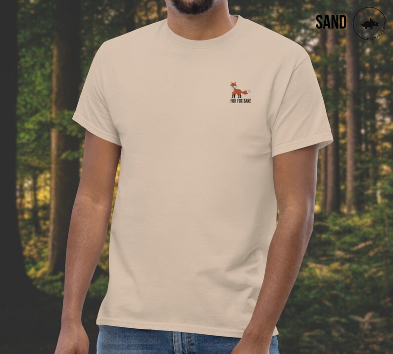 Puede incluir: Una camiseta beige con un peque&ntilde;o gr&aacute;fico de zorro y el texto "For Fox Sake" impreso en la parte delantera.
