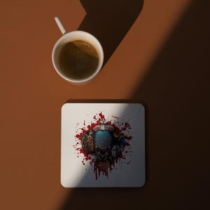 May include: White ceramic coaster with a red, white, and blue graphic of a clown's face surrounded by blood splatters.
