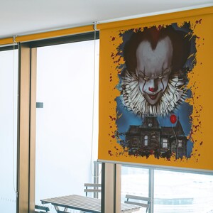 May include: A yellow window blind with a graphic of a scary clown with a red balloon and a house in the background.