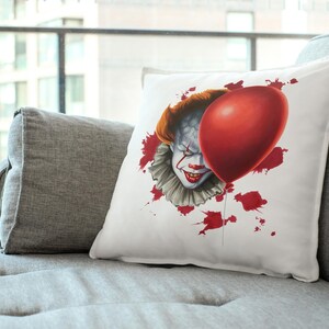May include: White pillow with a red balloon and a clown face with red paint splatters. The clown is wearing a white collar and has a sinister expression.