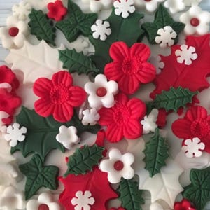May include: A close-up of a festive arrangement featuring red and white flowers, green holly leaves, and white snowflake-shaped accents. The arrangement is set against a white background, creating a vibrant and celebratory display, perfect for holiday decorations.
