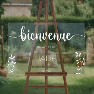 Könnte beinhalten: Ein klares Acryl-Willkommensschild mit weißer Kalligraphie, auf dem "bienvenue au baptême de JADE 02.09.23" steht. Das Schild ist auf jeder Seite mit weißen Blumenzweigen verziert.