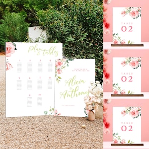 May include: Wedding table number sign with a floral design featuring pink roses and green leaves. The sign is white with pink text that reads "TABLE 02".