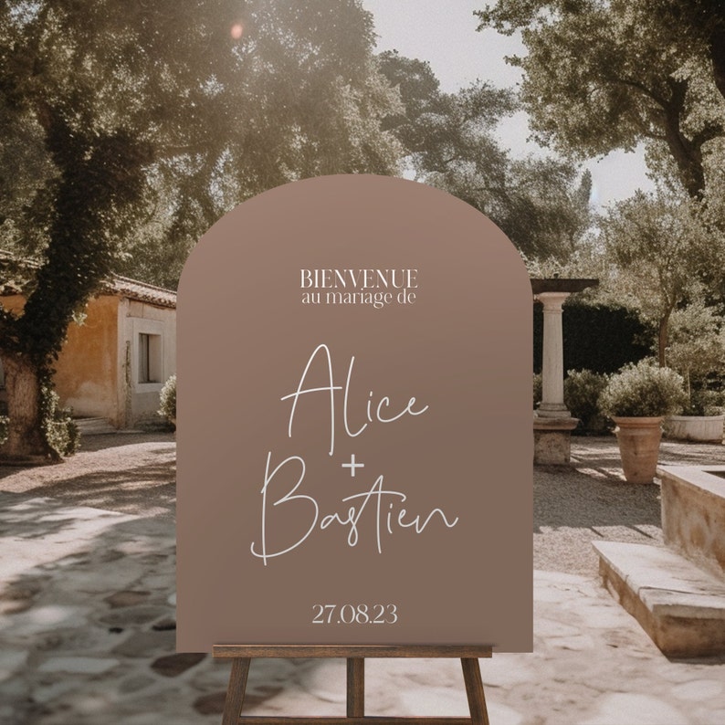 May include: A brown welcome sign with a rounded arch top. The sign says "Bienvenue au mariage de Alice + Bastien 27.08.23".